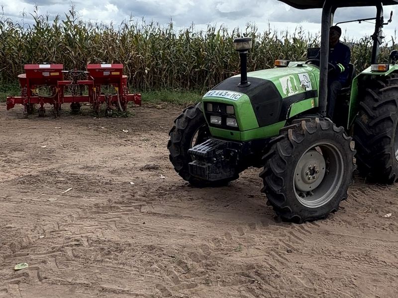 Trator com semeadora junto a um campo de milho